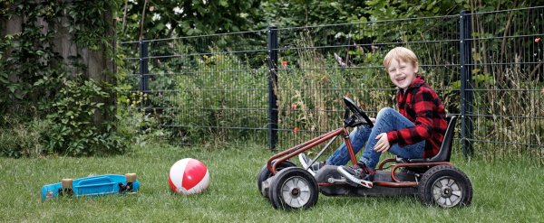 Kind sitzt im Garten auf einem Kettcar.