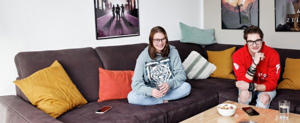 Zwei Jugendliche schauen auf dem Sofa gemeinsam Fernsehen.