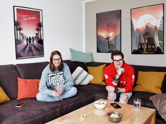 Zwei Jugendliche schauen auf dem Sofa gemeinsam Fernsehen.