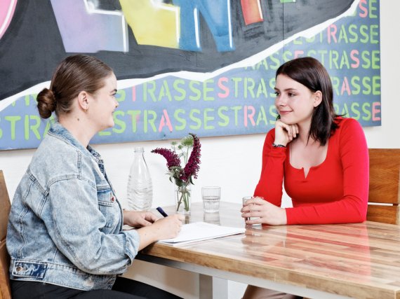 Mitarbeiterin und Klientin sitzen am Tisch und unterhalten sich.