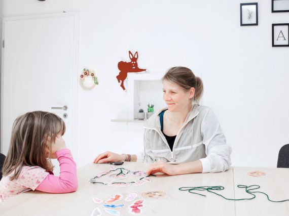 Mitarbeiterin und Kind basteln mit Schnüren und Papier.