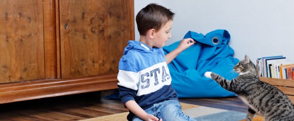 Kind sitzt mit Katze auf Teppich.