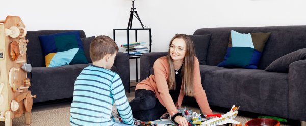 Mitarbeiterin und Kind sitzen auf dem Boden und spielen mit Bausteinen.