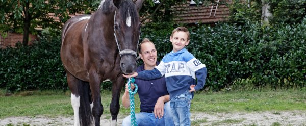 Kind füttert ein Pferd. Betreuer kniet daneben.