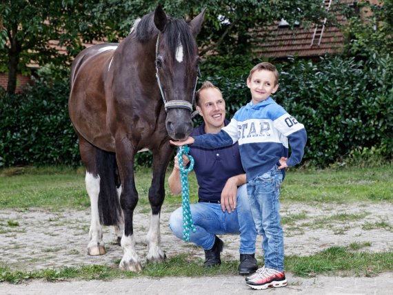 Kind füttert ein Pferd. Betreuer kniet daneben.