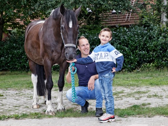 Kind füttert ein Pferd. Betreuer kniet daneben.