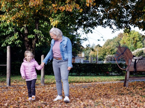 Mitarbeiterin und Kind gehen Hand in Hand über laubbedeckten Boden.