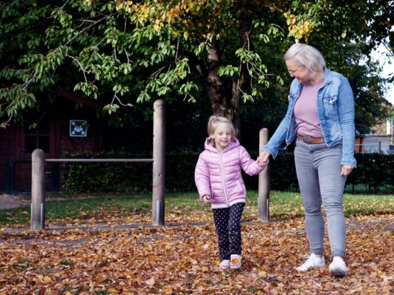 Mitarbeiterin und Kind gehen Hand in Hand über laubbedeckten Boden.