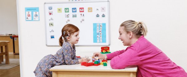 Kind mit sichtbarem Cochlea-Implantat und Erzieherin beim Spiel mit Lego.