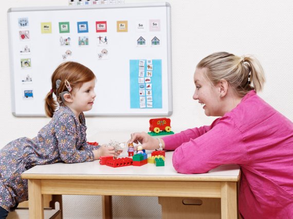 Kind mit sichtbarem Cochlea-Implantat und Erzieherin beim Spiel mit Lego.