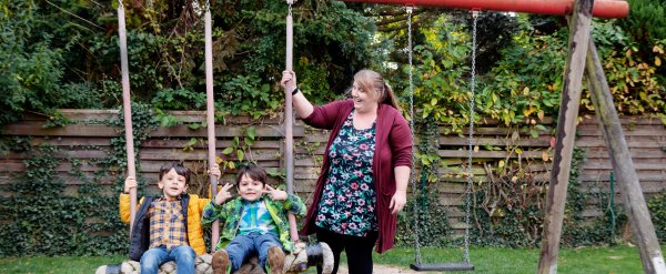 Mitarbeiterin gibt zwei Kindern auf der Schaukel Anschwung.