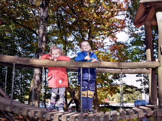 Zwei Kinder stehen auf dem Spielplatz auf einer Holzbrücke.