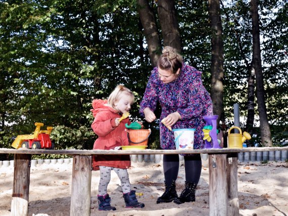 Mitarbeiterin und Kind spielen im Sandkasten.