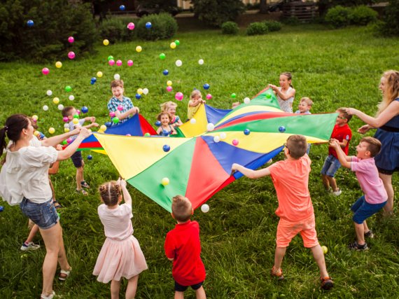 Erzieherinnen und Kinder halten ein großes Tuch und werfen damit Bälle in die Luft.