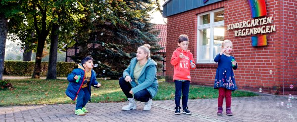 Kinder und Erzieherin spielen mit Seifenblasen auf dem Hof der Kita Schallenbach.