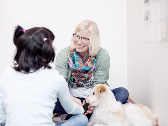 Logopädin, Mädchen und Therapiehund sitzen auf dem Boden.
