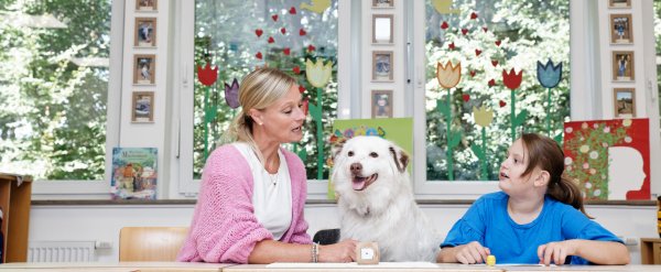 Lehrkraft und Schülerin spielen Lese-Lernspiel. Ein Hund sitzt zwischen ihnen.