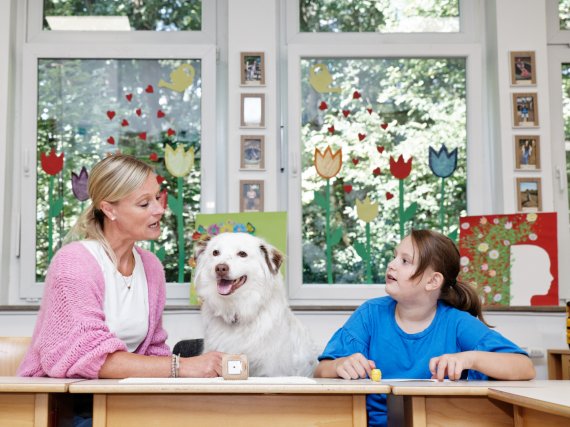 Lehrkraft und Schülerin spielen Lese-Lernspiel. Ein Hund sitzt zwischen ihnen.