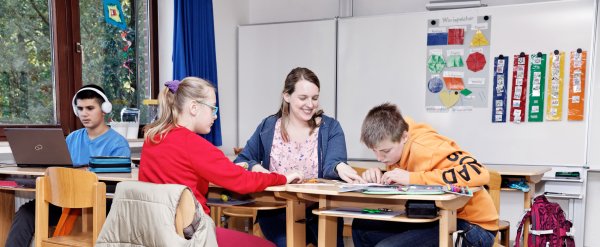 Lehrerin hilft Schülerinnen und Schülern bei Schulaufgaben.