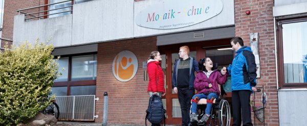 Gruppe aus Schülerinnen und Schülern steht vor dem Gebäude der Mosaik-Schule.