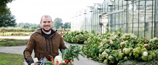 Mann trägt eine Kiste mit Gemüse.