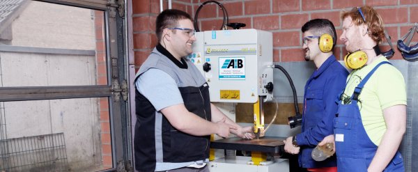 Mitarbeiter leitet zwei Beschäftigte an der Metallbandsäge an.