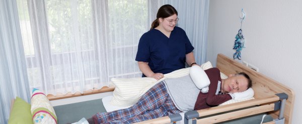 Mitarbeiterin lagert Bewohner um Bett um.