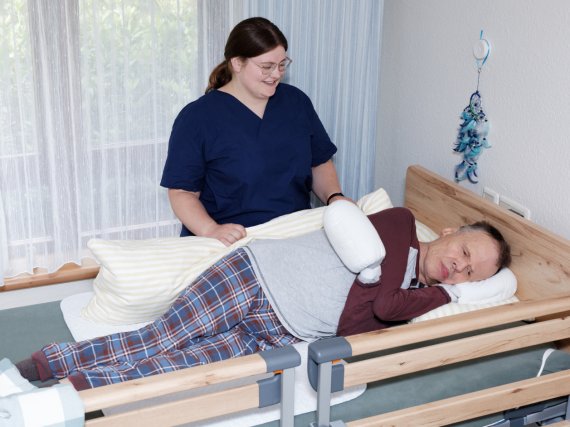 Mitarbeiterin lagert Bewohner um Bett um.
