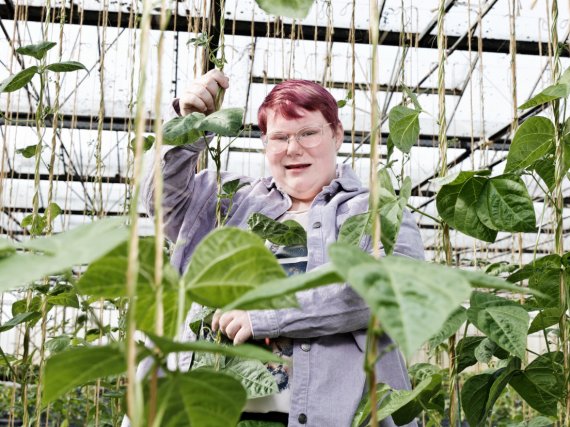 Beschäftigte steht im Gewächshaus zwischen hohen Ranken.