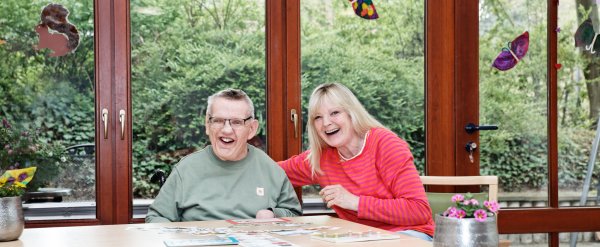 Bewohner und Betreuerin lachen beim Kartenspiel.