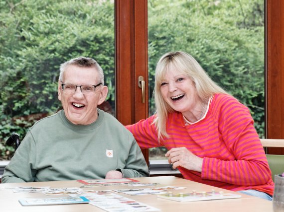 Bewohner und Betreuerin lachen beim Kartenspiel.