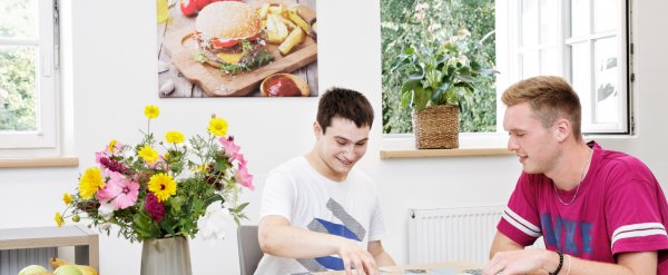 Mitarbeiterin und junger Klient machen Motorik-Übungen mit kleinen Gegenständen aus Holz und Metall.