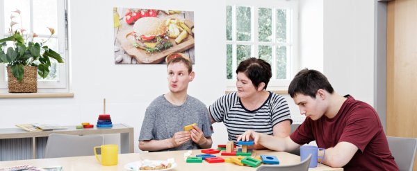 Mitarbeiterin und zwei Bewohner spielen mit bunten Bauklötzen.