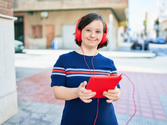 Junge Frau mit Down-Syndrom trägt Kopfhörer und hält Tablet in der Hand.