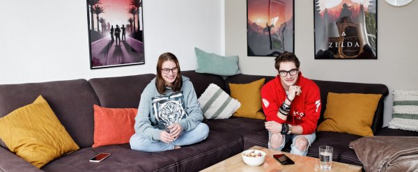 Zwei Jugendliche schauen auf dem Sofa gemeinsam Fernsehen.