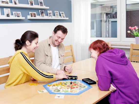 Mitarbeiter und zwei Kinder spielen ein Gesellschaftsspiel.