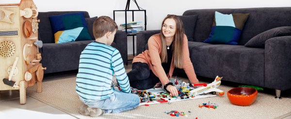 Mitarbeiterin und Kind sitzen auf dem Boden und spielen mit Bausteinen.