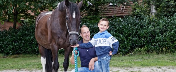 Kind füttert ein Pferd. Betreuer kniet daneben.