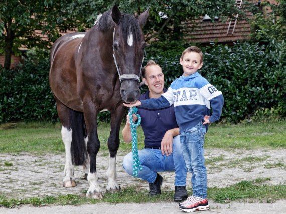 Kind füttert ein Pferd. Betreuer kniet daneben.