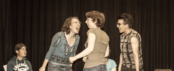 Eine Szene aus einem Theaterstück. Drei Frauen auf der Bühne schreien sich an.
