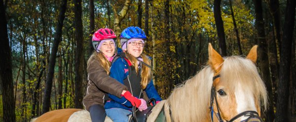 Zwei Mädchen sitzen gemeinsam auf einem Pferd.