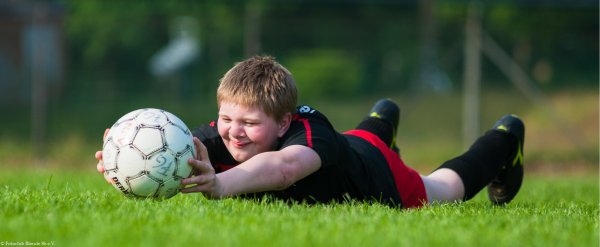 Junge liegt auf dem Fußballplatz und hält Fußball in den Händen