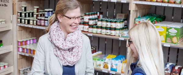 Anleiterin und Auszubildenden stehen im Laden vor einem Warenregal.