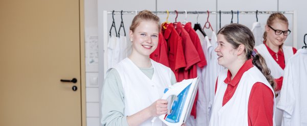 Hauswirtschafterin steht mit Beschäftigter an einem Bügelbrett und hält ein Bügeleisen