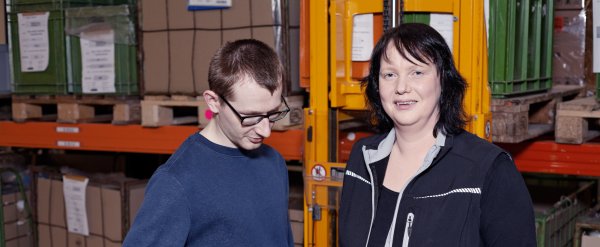 Wirtschaftswirtin zeigt einem Beschäftigten die Bedienung eines Handhubwagens.