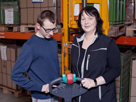 Wirtschaftswirtin zeigt einem Beschäftigten die Bedienung eines Handhubwagens.