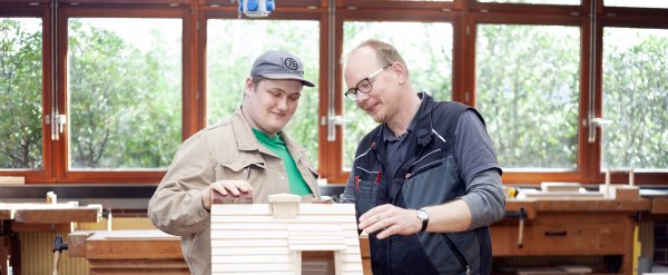 Tischler und Beschäftigter schmirgeln Vogelhaus in Holzwerkstatt.