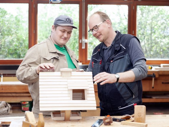 Tischler und Beschäftigter schmirgeln Vogelhaus in Holzwerkstatt.