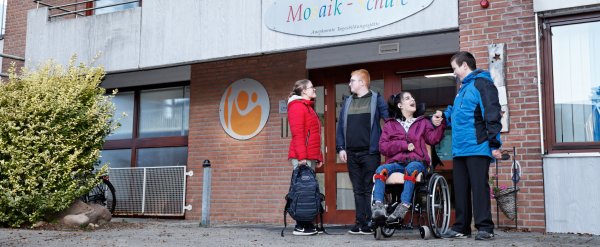 Gruppe aus Schülerinnen und Schülern steht vor dem Gebäude der Mosaik-Schule.