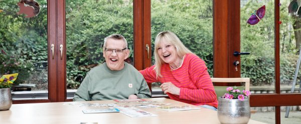 Bewohner und Betreuerin lachen beim Kartenspiel.